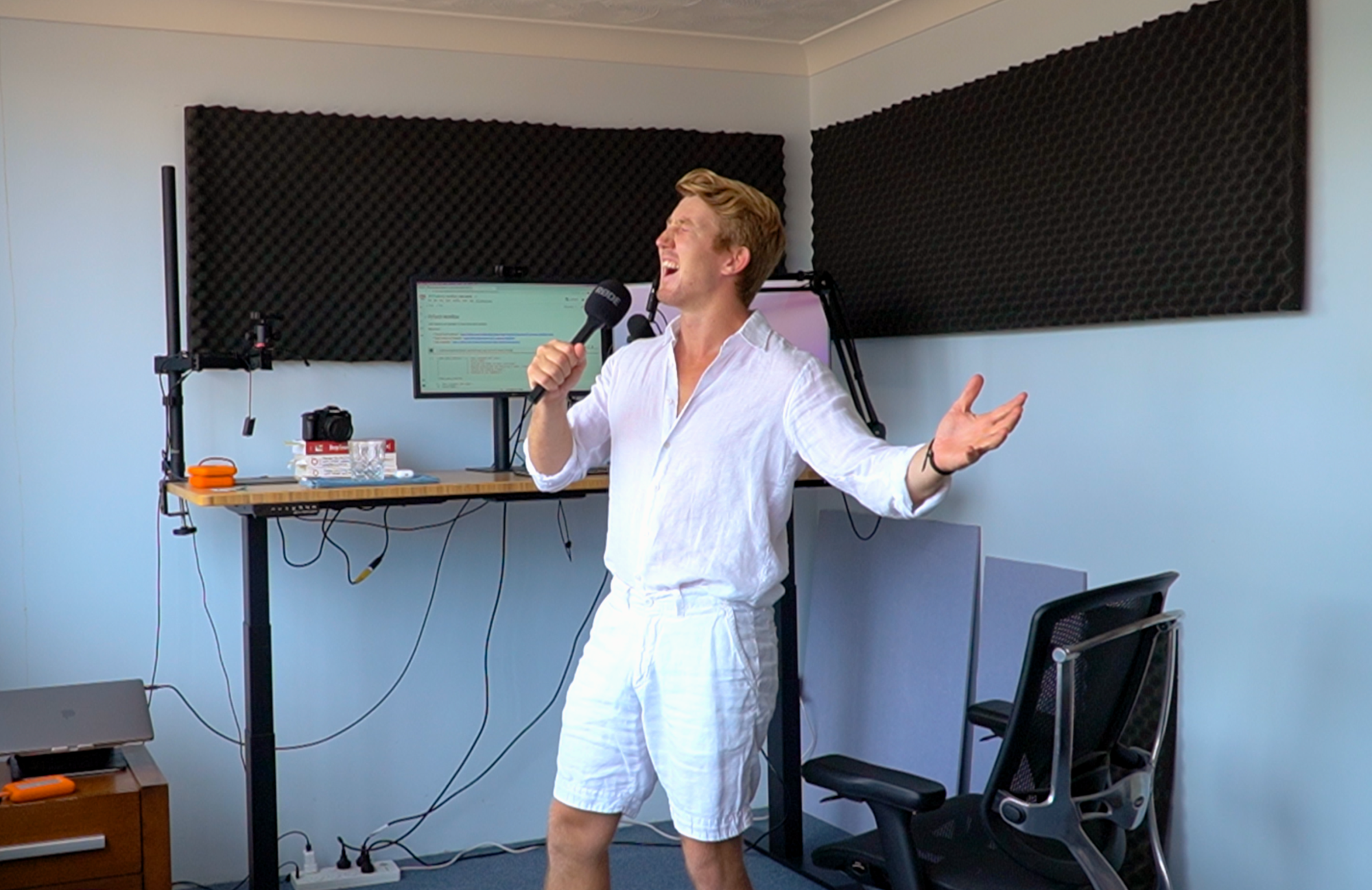 man standing in computer studio with microphone in hand and screens behind singing a song
