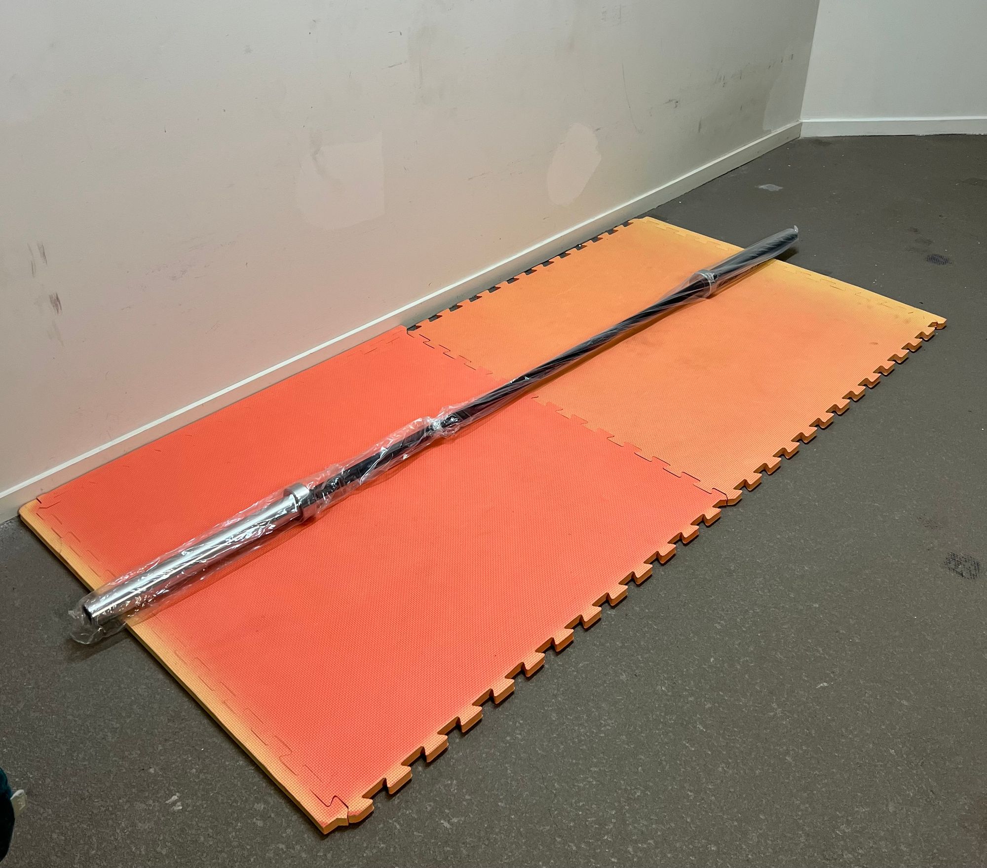 Weightlifting bar on an orange foam mat in front of a white wall
