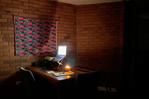 laptop on desk with writing notepad next to it candle burning to create light against wall, flamingo poster on wall