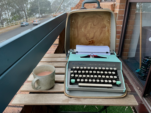 cup of tea and typewriter on small wooden table on balcony with view of trees and water