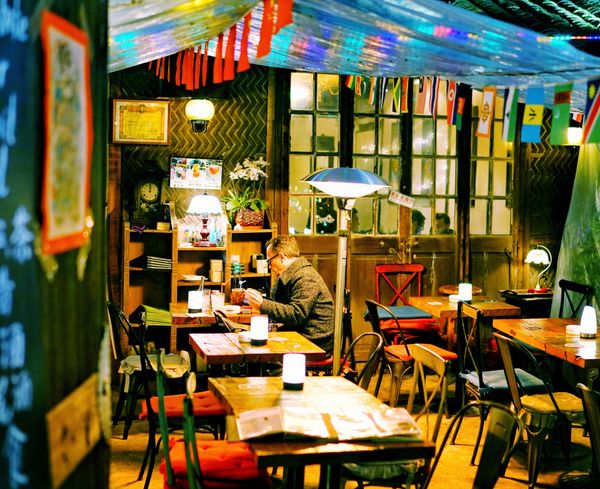 Man sitting at a table alone with coloured chairs around the room and bright lights on every table