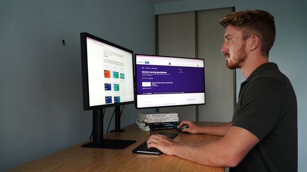 man looking at two computer screens with hand on keyboard, focus is on the left screen